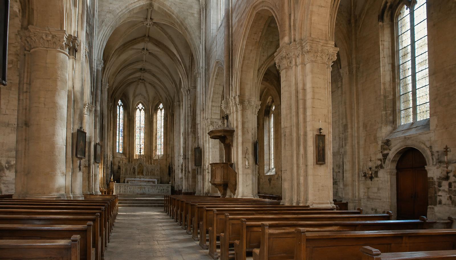Interior of a stone cathedral nave with wooden pews